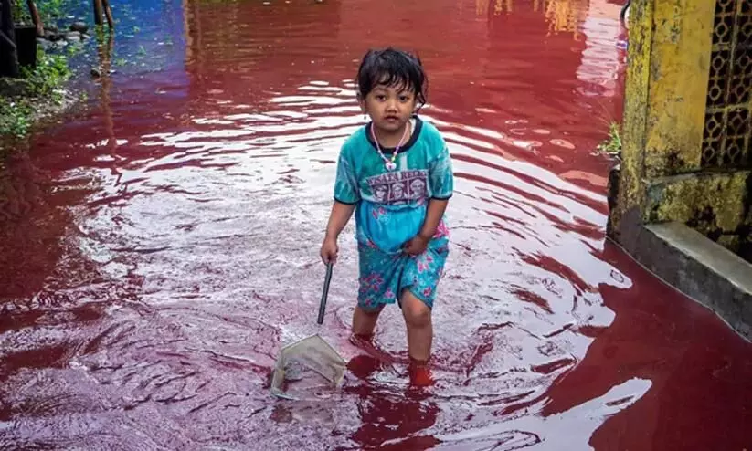 A girl walks through a flooded road with red water i
