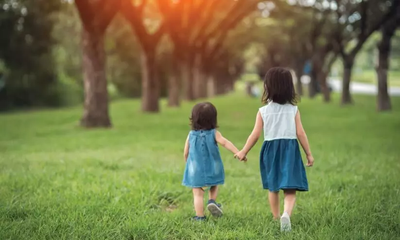 two kids held hands and walking through meadow