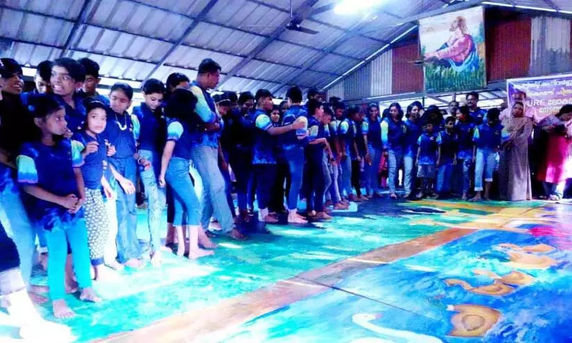 പ​രി​സ്ഥി​തി സം​ര​ക്ഷ​ണ സ​ന്ദേ​ശ​വു​മാ​യി അ​ധ്യാ​പ​ക​നും വി​ദ്യാ​ർ​ഥി​ക​ളും ചേ​ർ​ന്ന് കാ​ലു​കൊ​ണ്ട് ചി​ത്രം വ​ര​ക്കു​ന്നു