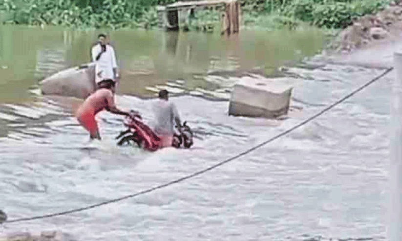 റോഡി​​​ലെ ഒഴുക്കിൽപ്പെട്ട് ബൈക്ക് യാത്രക്കാർ പുഴയിലേക്ക് വീണു