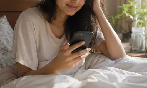 A person reaching for their smartphone on a bedside table immediately after waking up in the morning