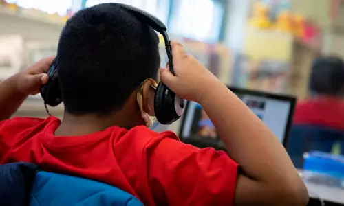 A young adult wearing earphones while working, illustrating safe volume and listening guidelines.