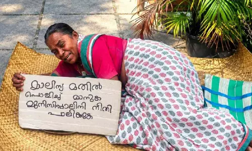 മാലിന്യത്തിൽ പൊറുതിമുട്ടി നഗരസഭ കവാടത്തിൽ പായവിരിച്ച് വീട്ടമ്മയുടെ സമരം മാലിന്യത്തിൽ പൊറുതിമുട്ടി നഗരസഭ കവാടത്തിൽ പായവിരിച്ച് വീട്ടമ്മയുടെ സമരം